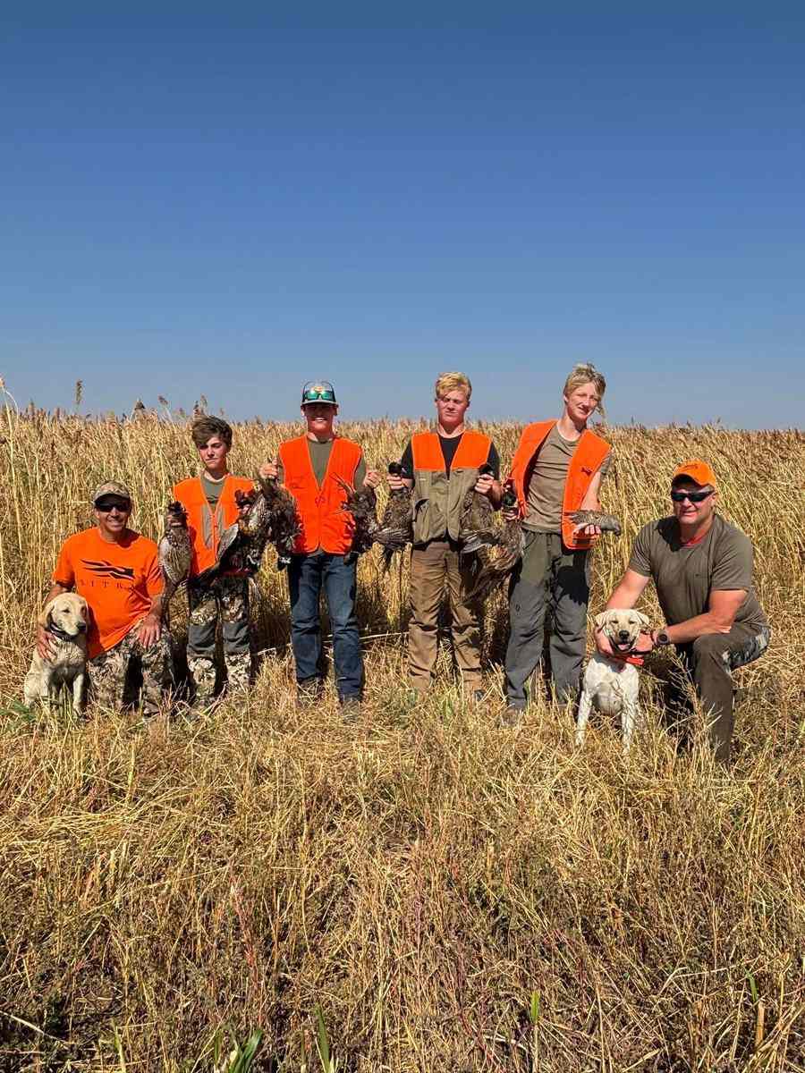 Group of five hunters in blaze orange with three bird dogs after a morning pheasant hunt